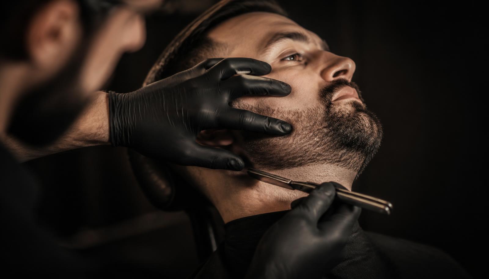 Barbeiro fazendo a barba de um cliente com navalha
